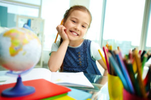 Young child smiling at a camera in a school desk setting.