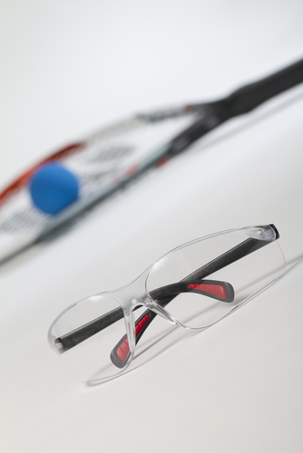 Protective glasses and an out of focus tennis racket, againist a gray background.