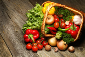 Overturned basket on a wooden floor. Out of the basket flow numerous fruits and vegetables.