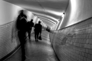 Distorted black and white image of people walking down a hall.