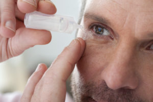 close up of a person applying eye drops to their eye.