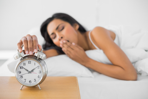 Person yawning as they hit the snooze button on an old fashioned alarm clock.