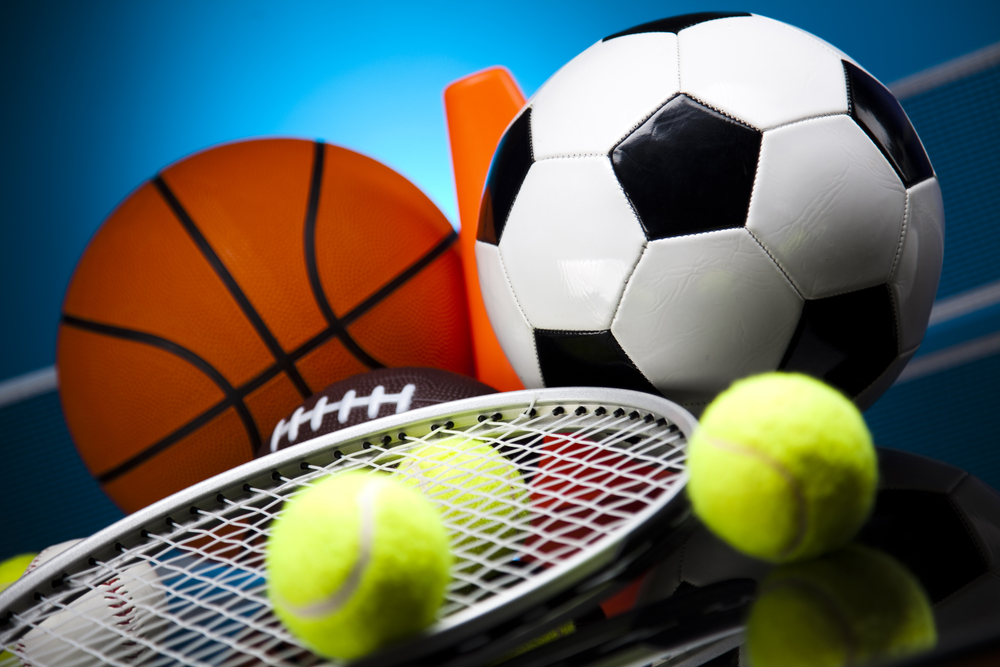 Assorted sports items, including a plastic orange cone, a basketball, a football, a soccer ball, a baseball, a tennis racket and 4 tennis balls.